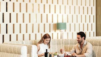 Ein modernes Interieur mit einer gemusterten Wand, einem Sofa, einem Tisch mit Lampe und einer kleinen Pflanze.