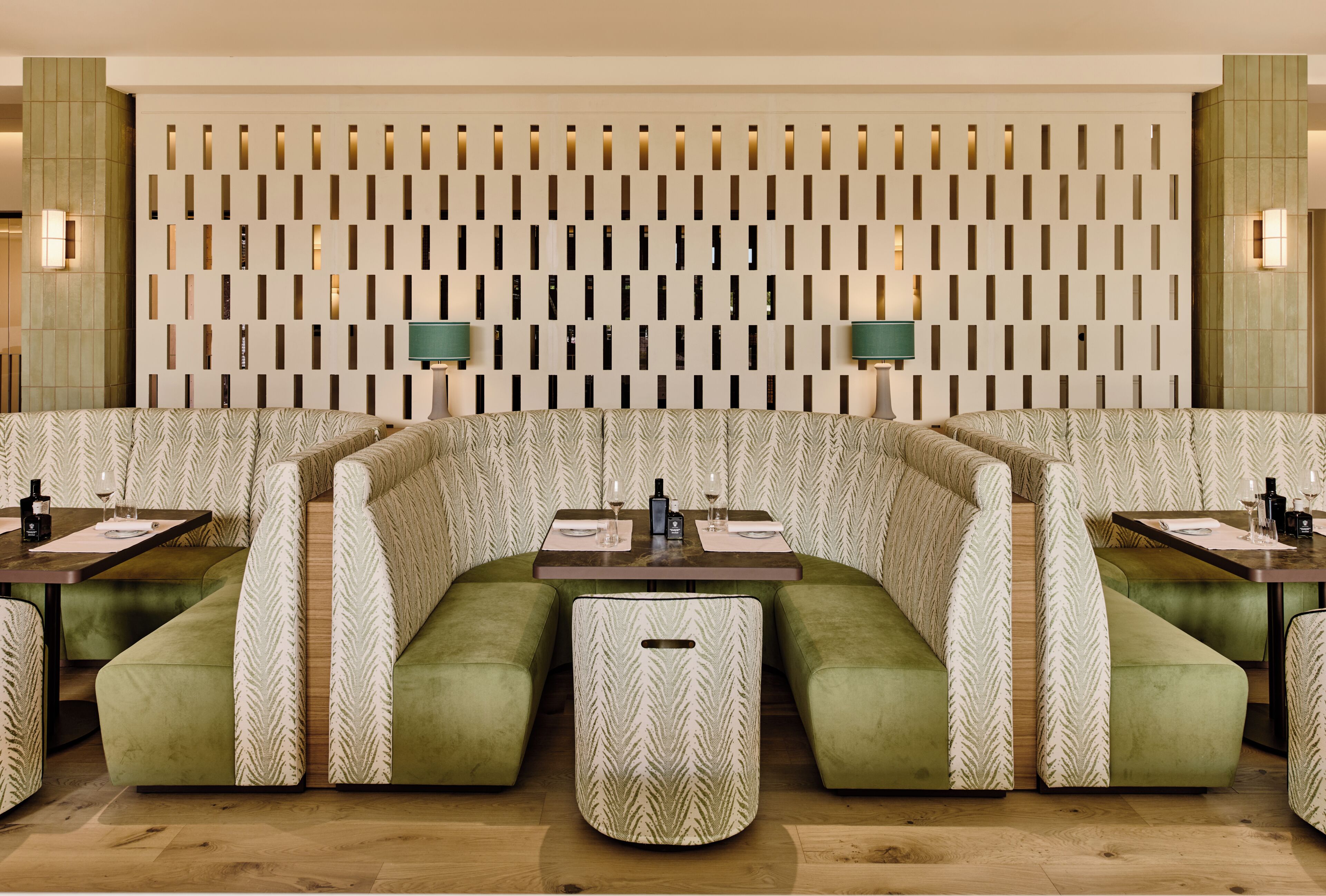 Un restaurante con diseño moderno, que presenta un patrón de pared único, asientos tapizados en verde y una mesa de comedor central.