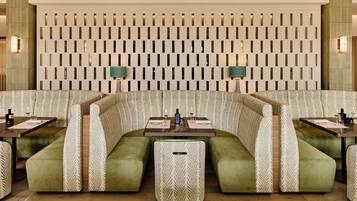 Un restaurante con diseño moderno, que presenta un patrón de pared único, asientos tapizados en verde y una mesa de comedor central.
