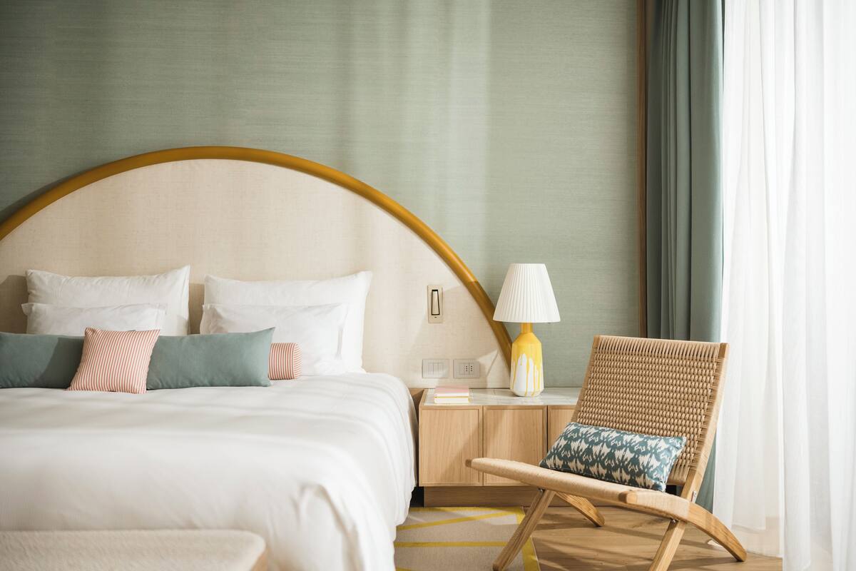 A neatly arranged hotel room with a large bed, a bedside table with a lamp, and a wicker chair.