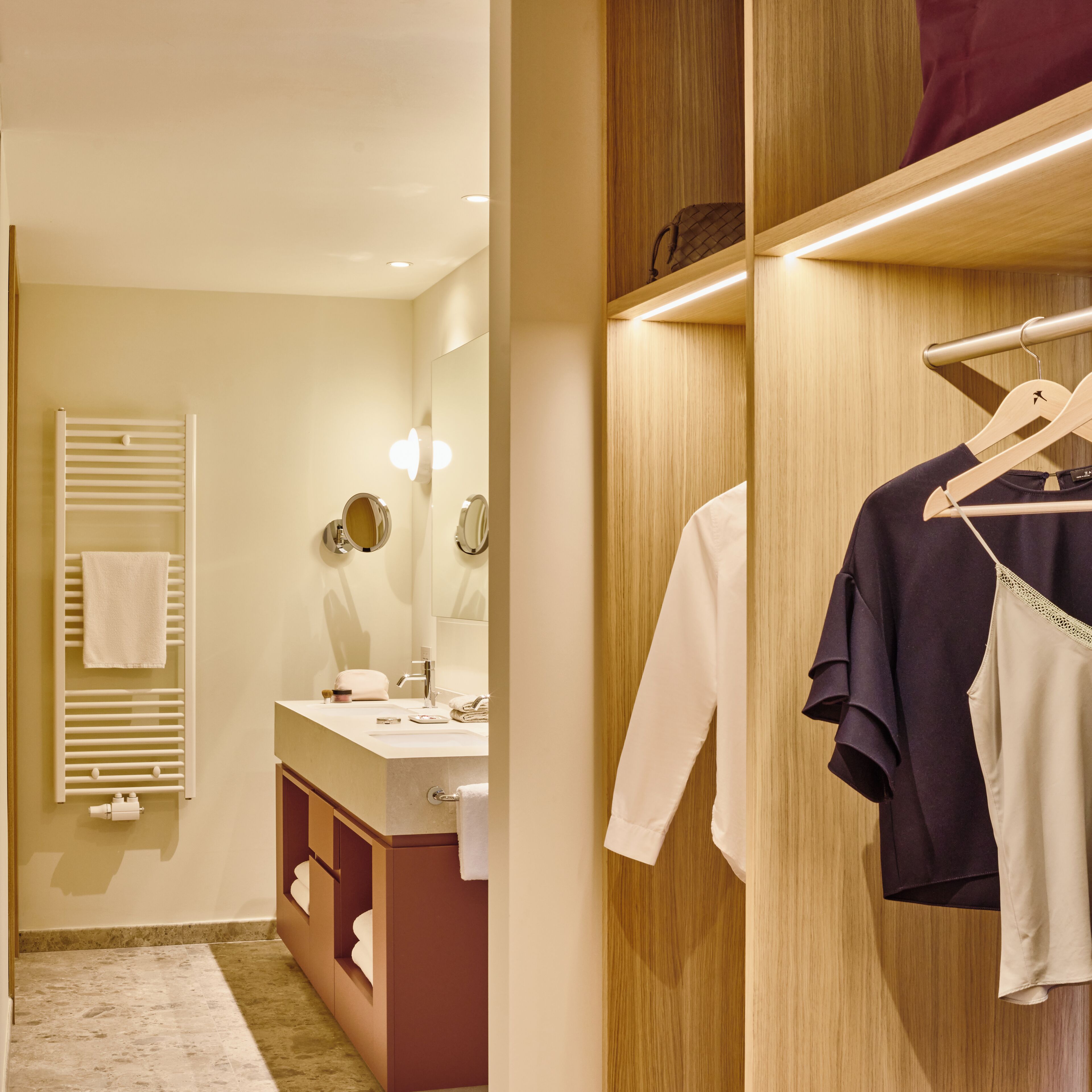 A modern bathroom with a vanity, mirror, towel rack, and wooden storage unit.