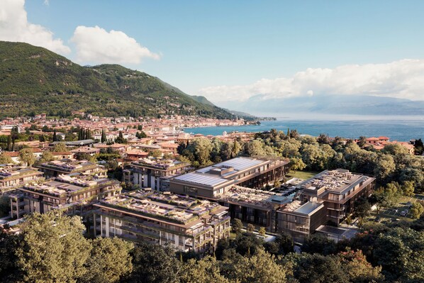 An aerial view of a coastal town with a mix of traditional and modern buildings, a marina, and a mountainous backdrop.