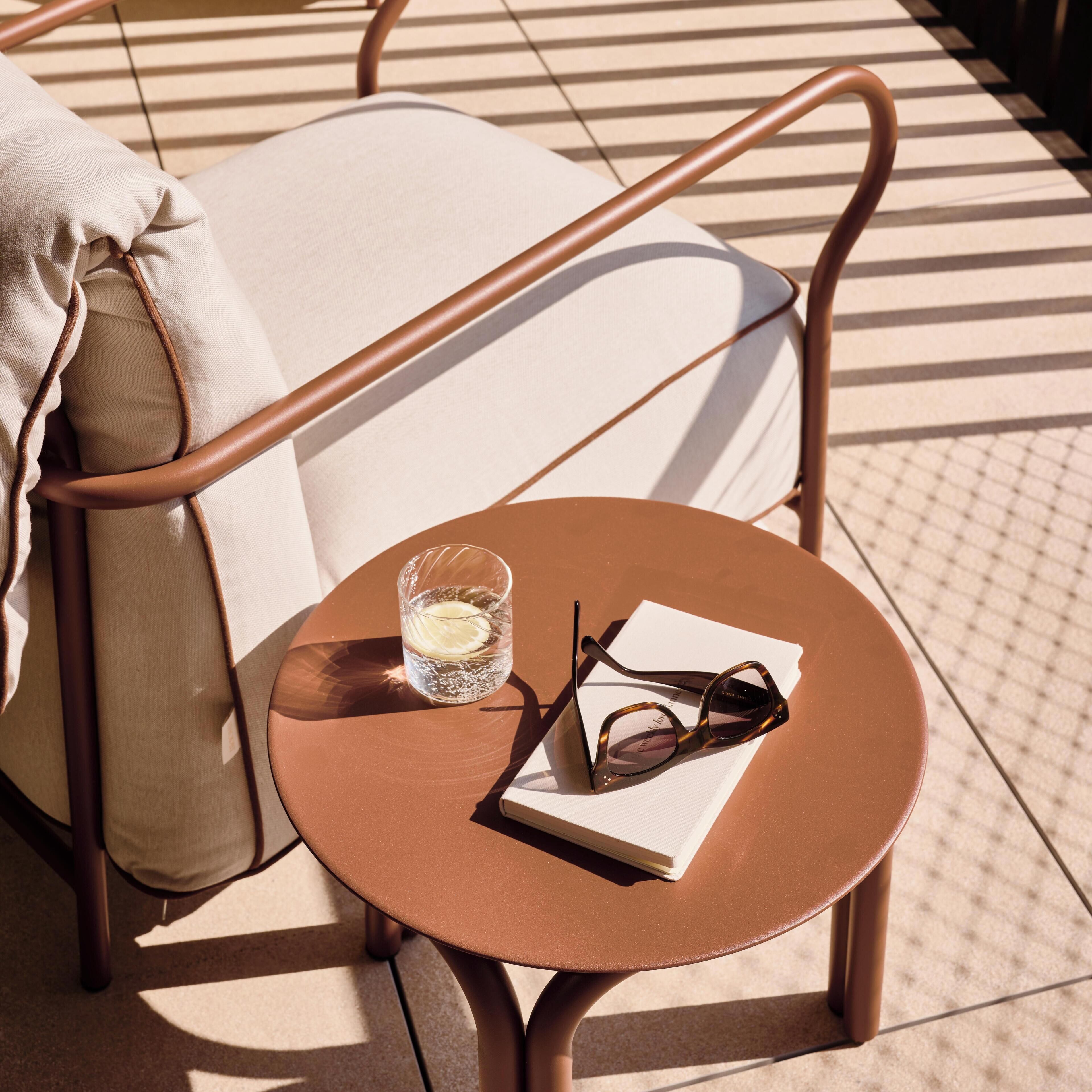A round table with a pair of glasses and a glass of water on it, a cushion on a chair, and a patterned floor.