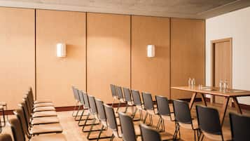 A conference room with a long table and rows of chairs, a door, and two wall-mounted light fixtures.