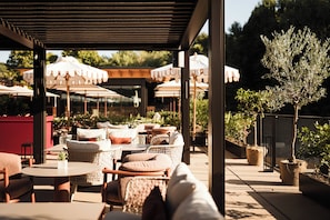 An outdoor seating area with tables and chairs, umbrellas, and potted plants. - Falkensteiner Resort Lake Garda (Salò)