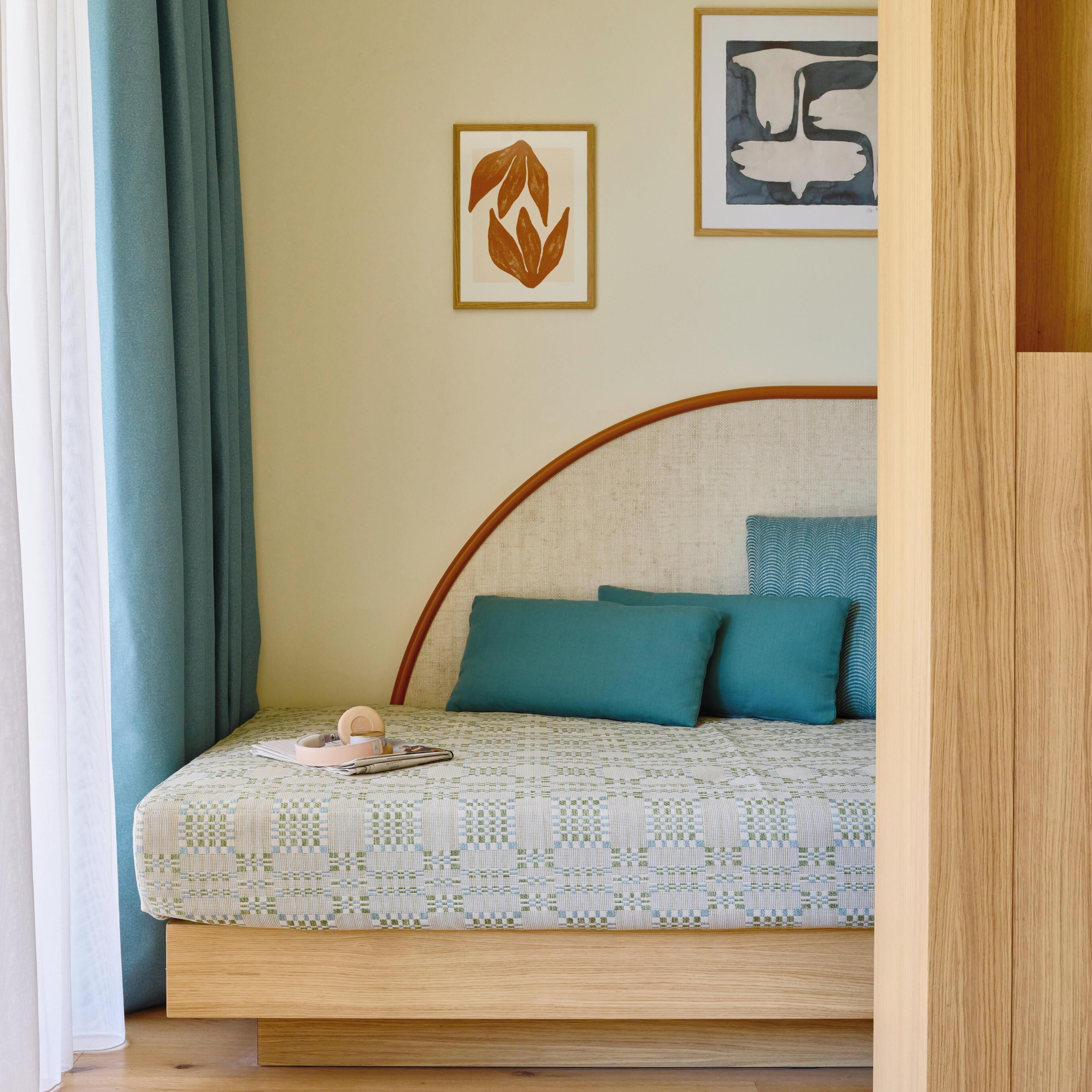 Een bed met een bedsprei met patroon, een hoofdbord en kussens. Twee kunstwerken hangen in de lijst op de muur.