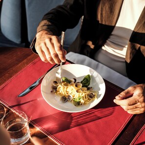 A person dining with a plate of pasta and clams, a fork, and a knife on a red placemat.