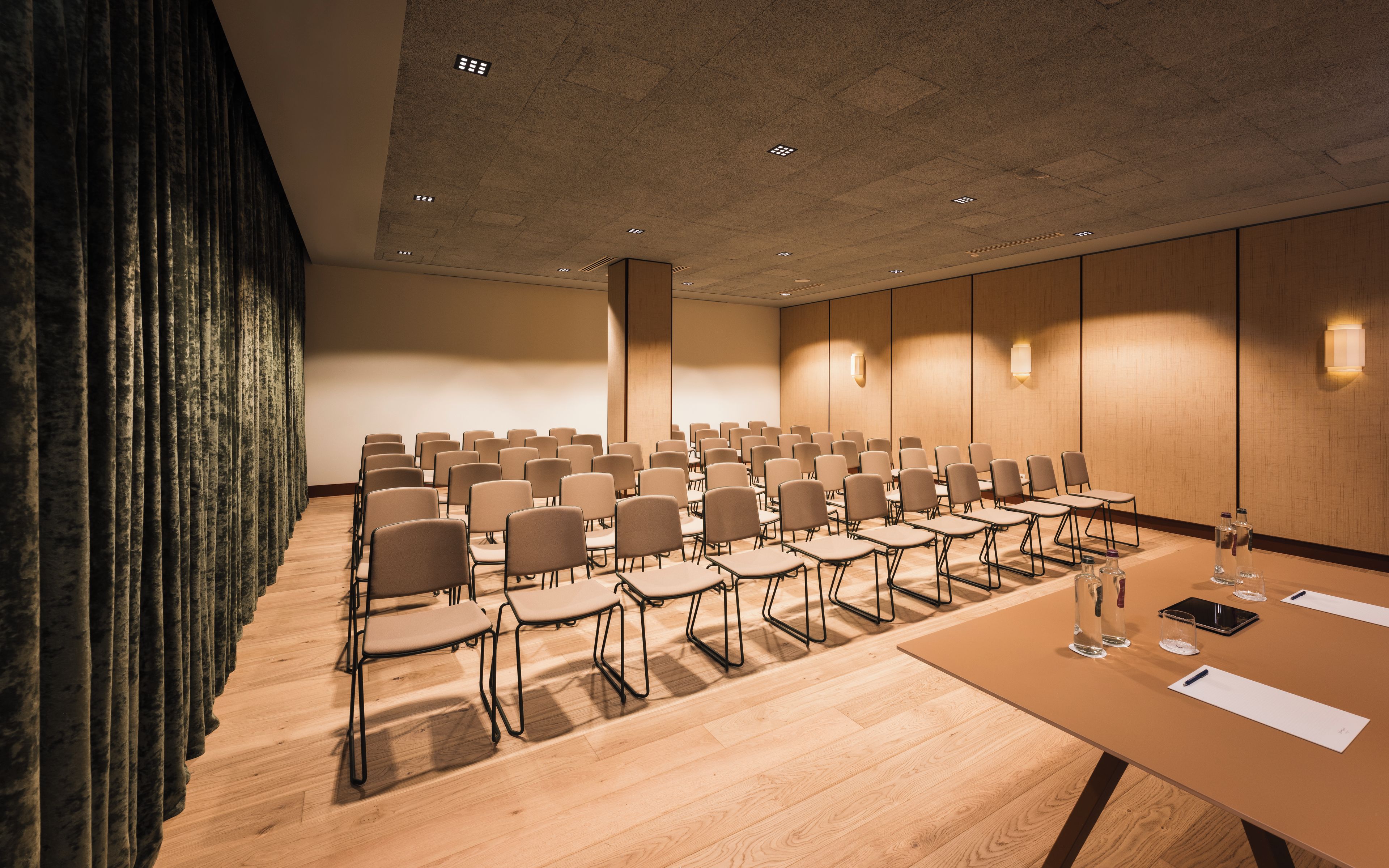 Ein Konferenzraum mit Reihen von Stühlen, einem langen Tisch und einem Holzboden.