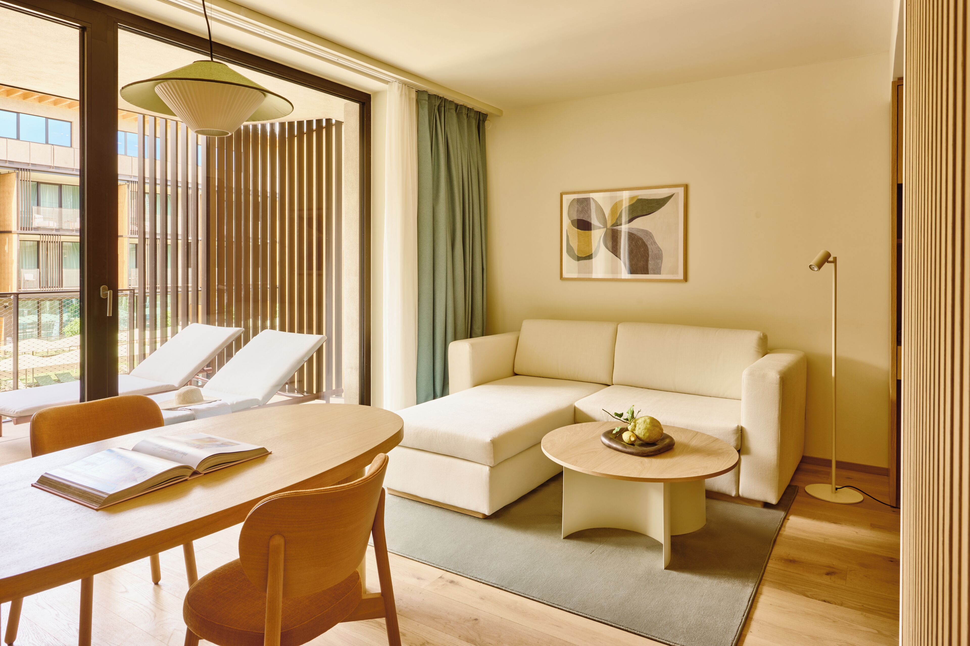 Una sala de estar moderna con un sofá, una mesa de comedor con sillas, una lámpara de pie y vistas al exterior.