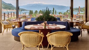 Una terraza con mesas redondas y sillas de mimbre, con vistas a un lago y montañas.