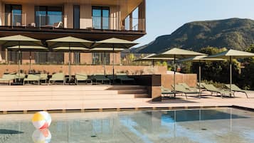 A pool area with lounge chairs and umbrellas, a clear sky, and a mountain in the background.