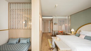 A hotel room with a bed, a bench, a desk, and a chair. There is a wooden floor and a partition with a lattice design.