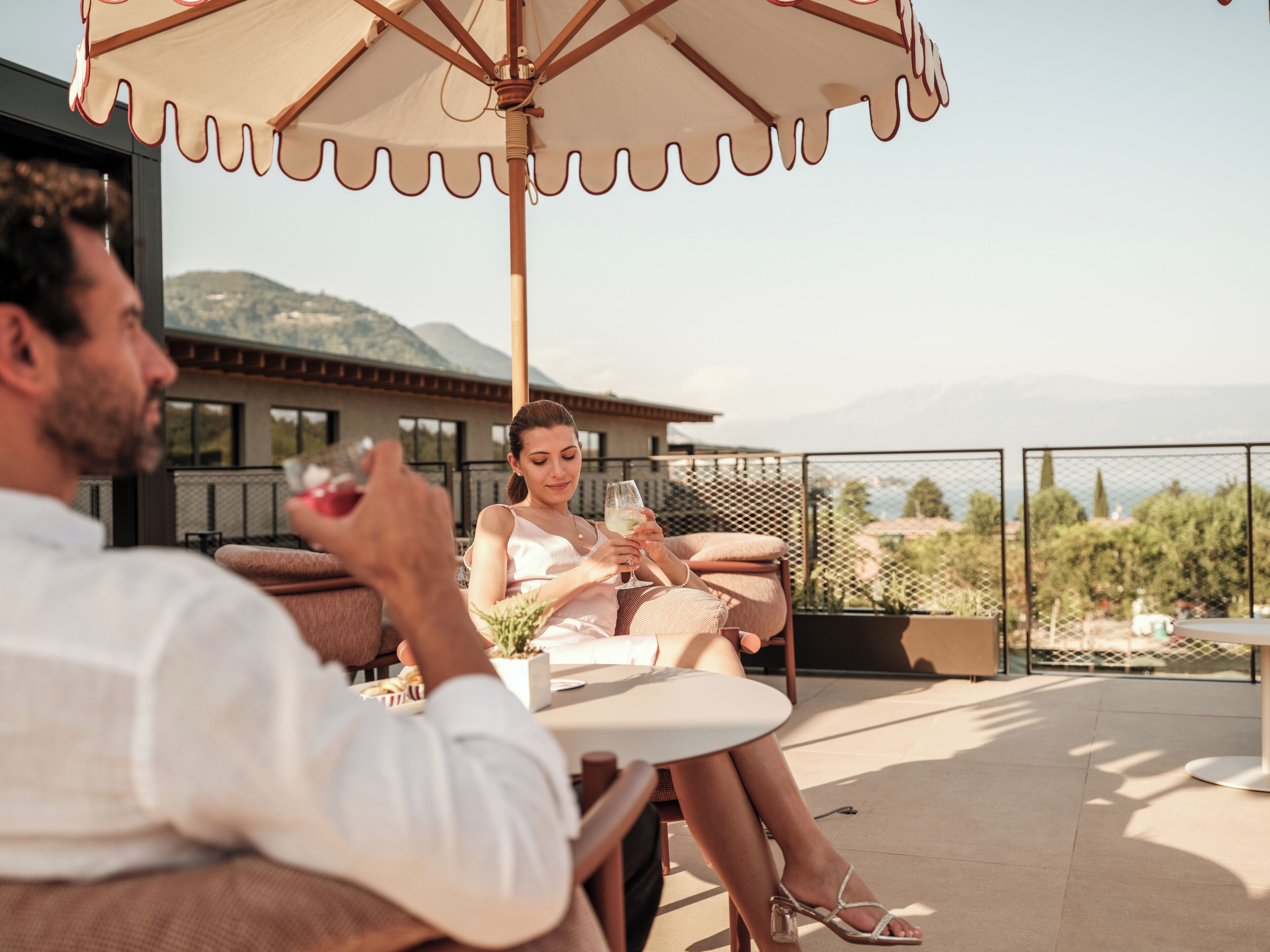 Un couple est assis à une table en plein air, avec une vue sur les montagnes et une maison en arrière-plan.