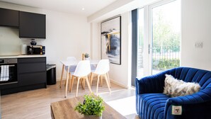 Une cuisine moderne avec des meubles de couleur sombre, un coin repas avec des chaises blanches et un canapé bleu agrémenté d’un coussin moelleux.