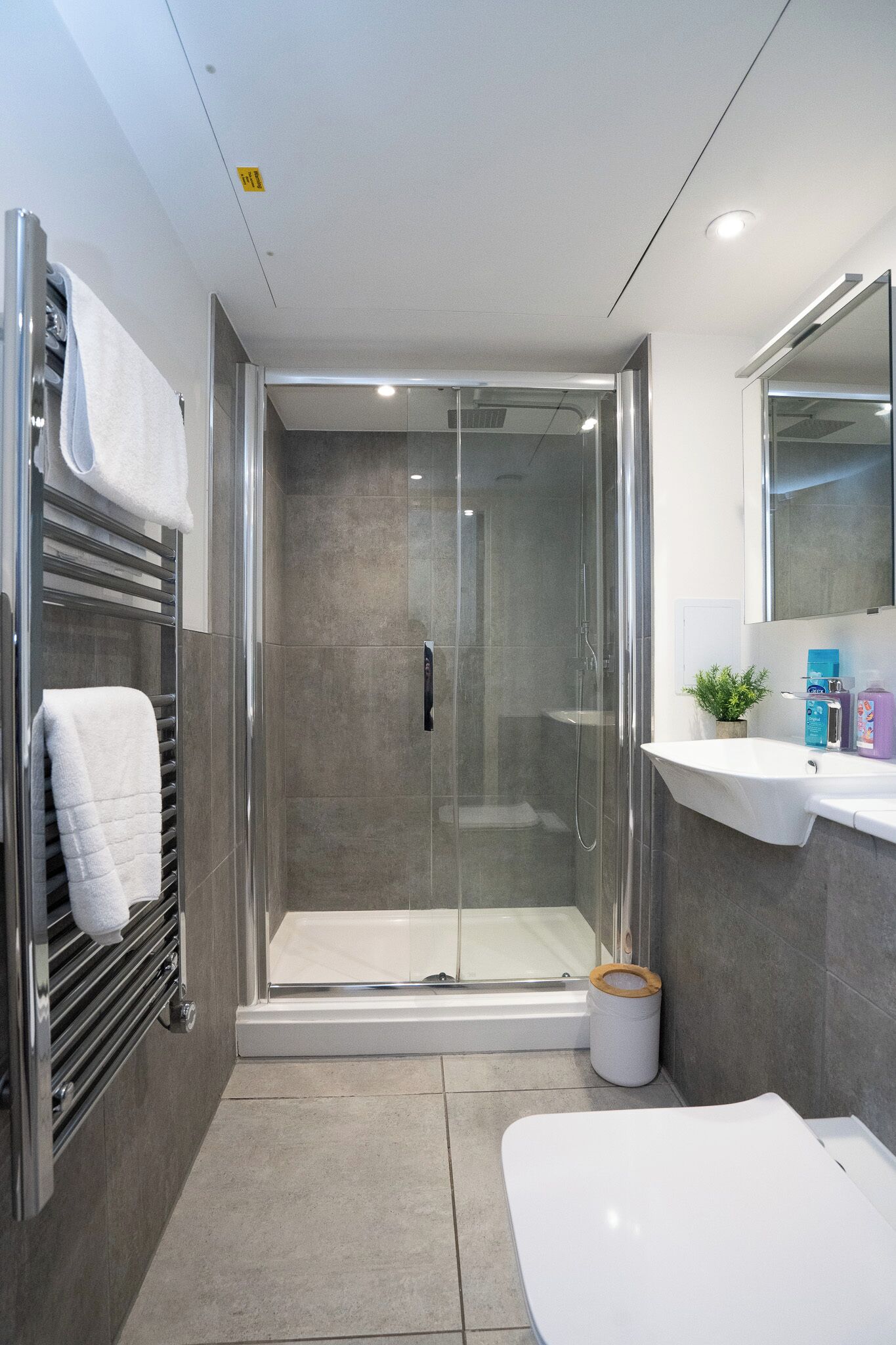 A modern bathroom with a glass-enclosed shower, a white sink, and a large mirror.