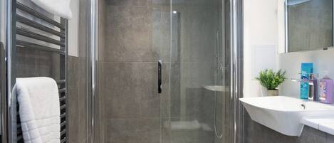 A modern bathroom with a glass-enclosed shower, a white sink, and a large mirror.
