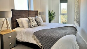 A modern bedroom with a large bed, two bedside tables, a window, and a plant. - Coates House by Guestz (Nailsea)