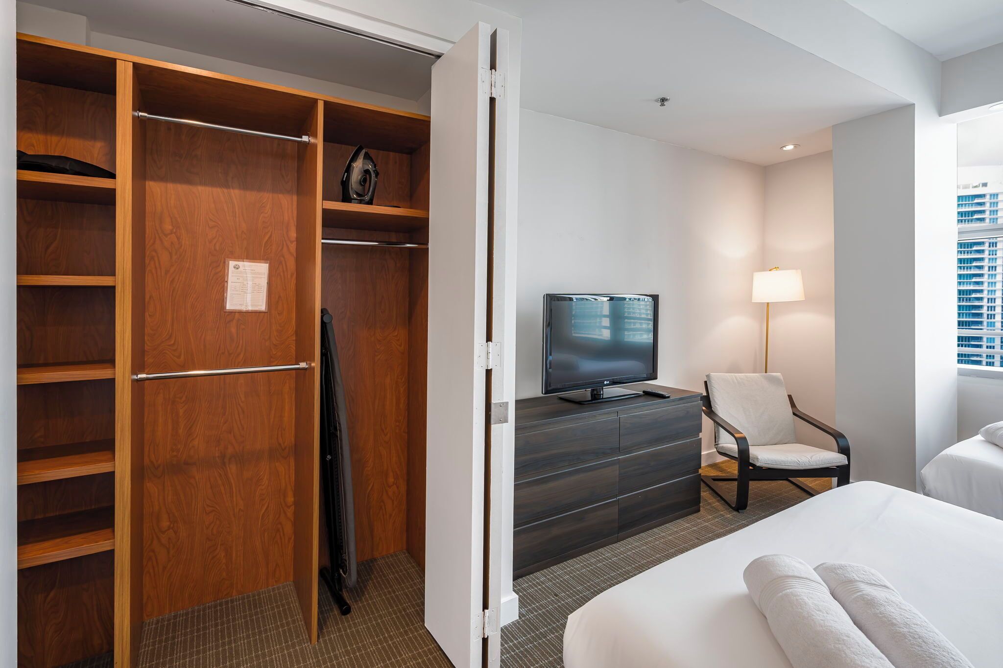 A hotel room with a wooden closet, a television on a dresser, a chair, and a bed.