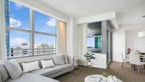 Ein modernes Hotelzimmer mit grauem Sofa, einem runden Couchtisch und Blick auf die Stadt durch große Fenster.