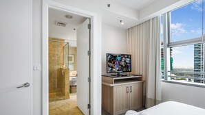 Ein Hotelzimmer mit Bett, Fernseher auf einem Holzboden, Badezimmer mit Duschkabine und Blick über die Stadt.