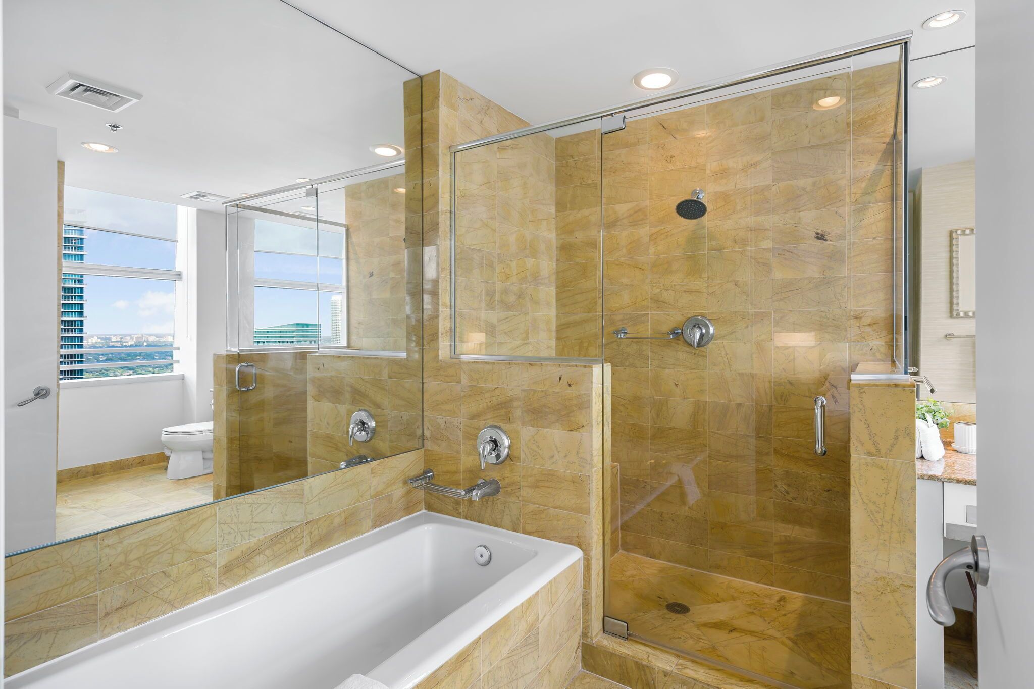 Un baño moderno con ducha envuelta en vidrio, una bañera grande y vistas a la ciudad a través de la ventana.