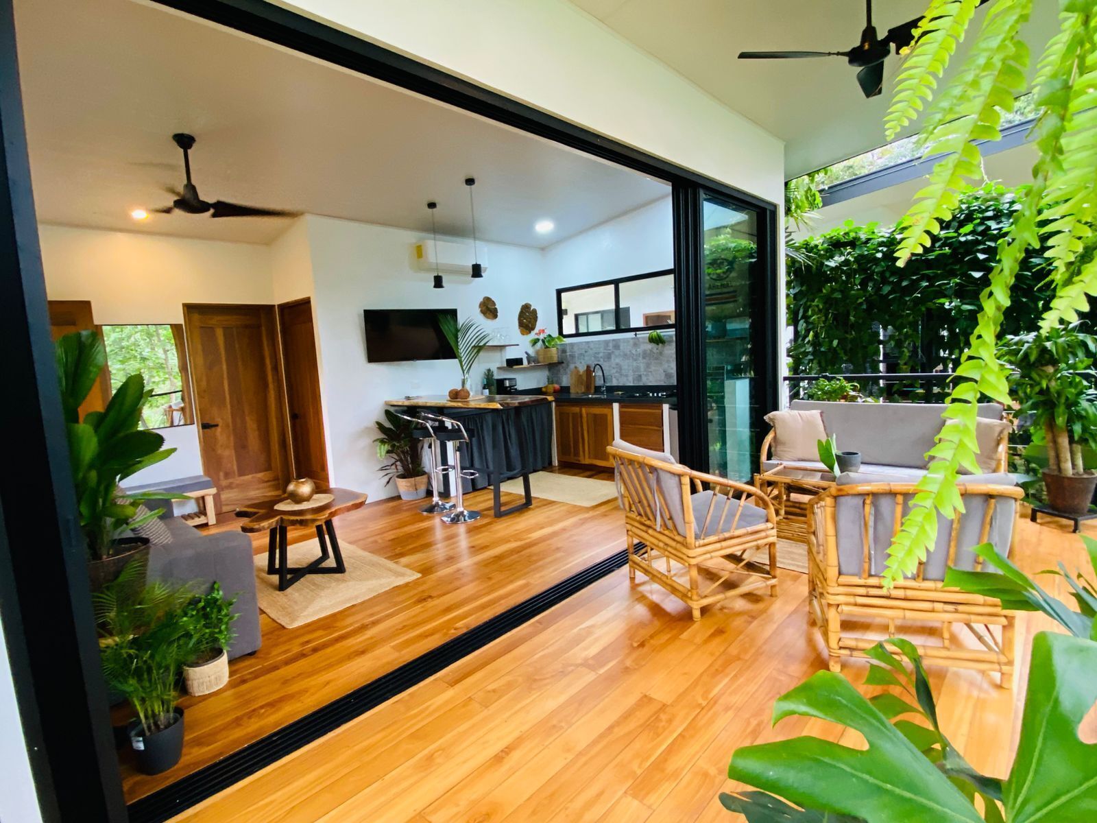 A modern interior with a kitchen, dining area, and a large sliding glass door leading to a balcony with plants.