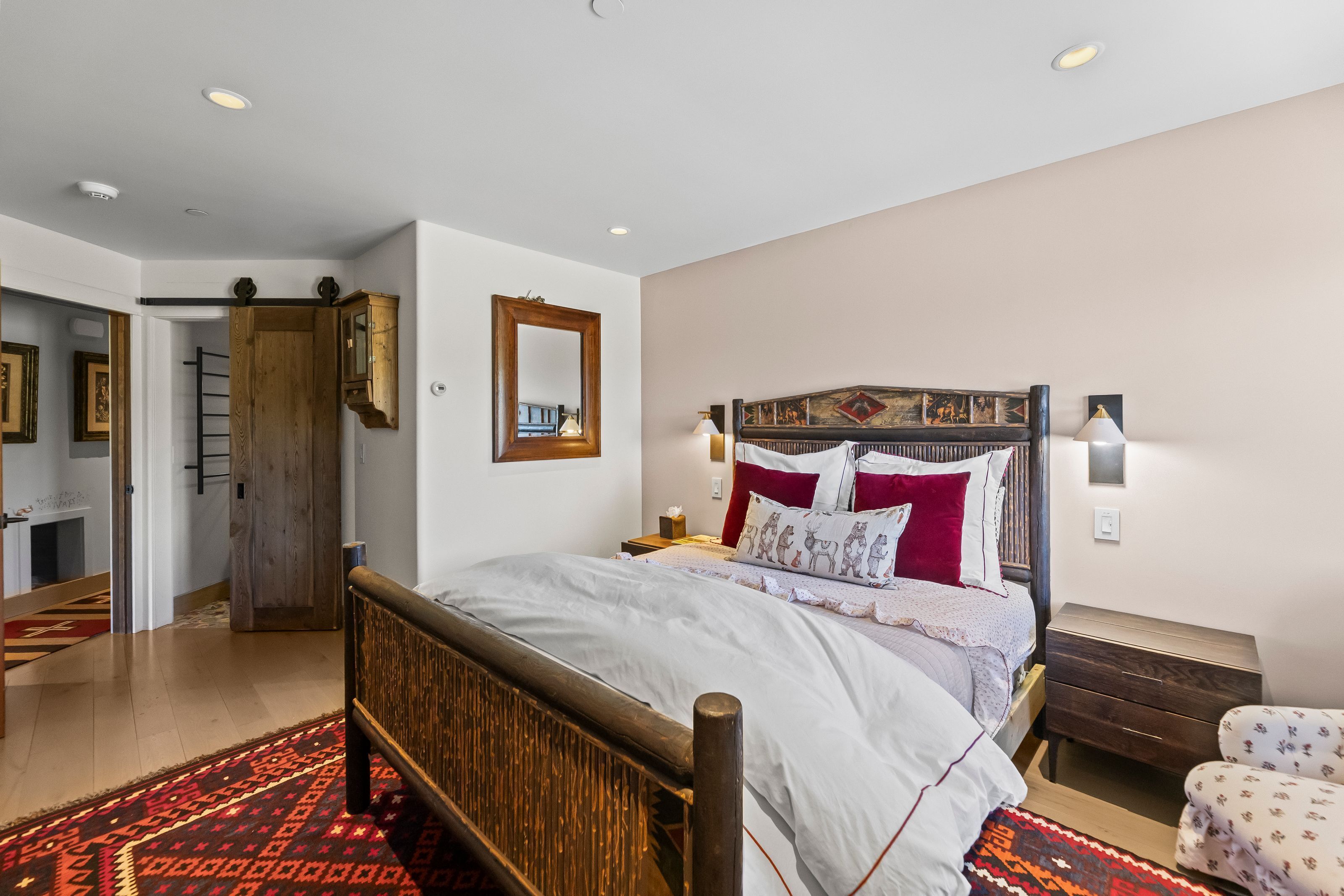 Une chambre à coucher avec un lit en bois, une table de chevet, une lampe fixée au mur et un tapis à motifs.