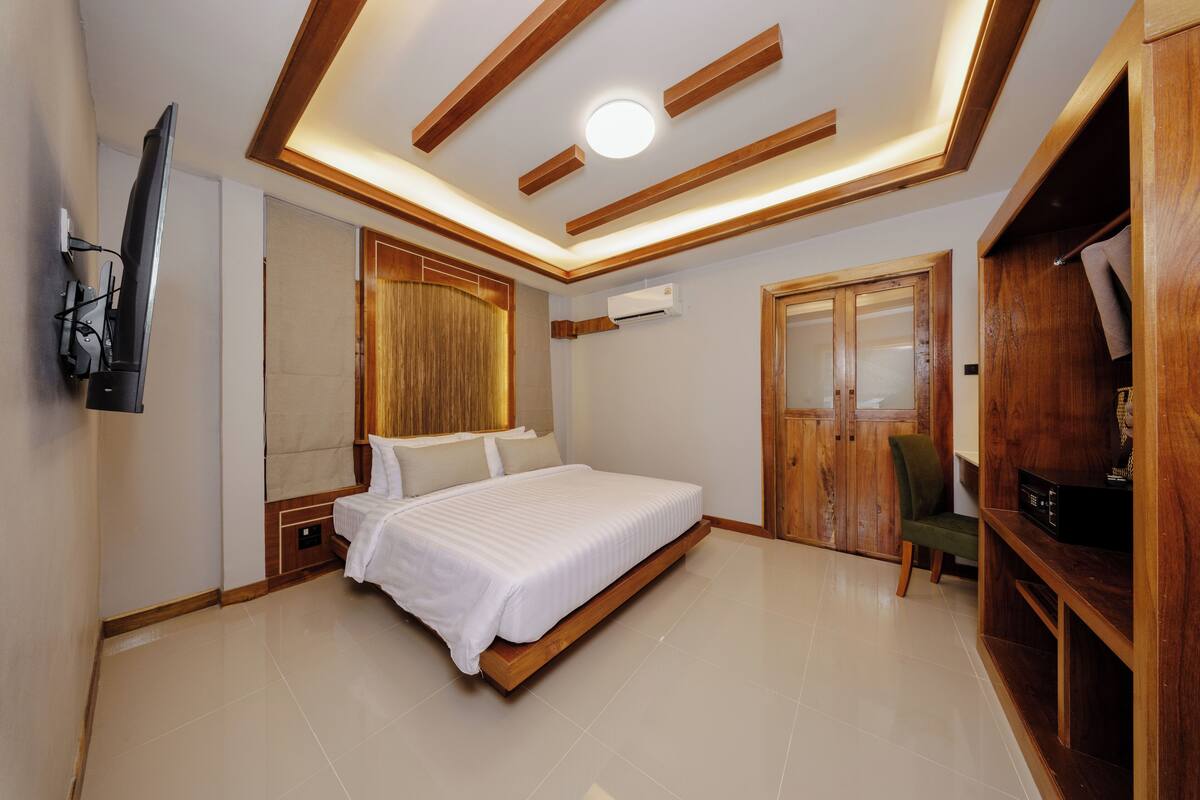 Een moderne slaapkamer met een groot bed, houten balken in het plafond, een flatscreen televisie aan de muur en een kledingkast met spiegel.