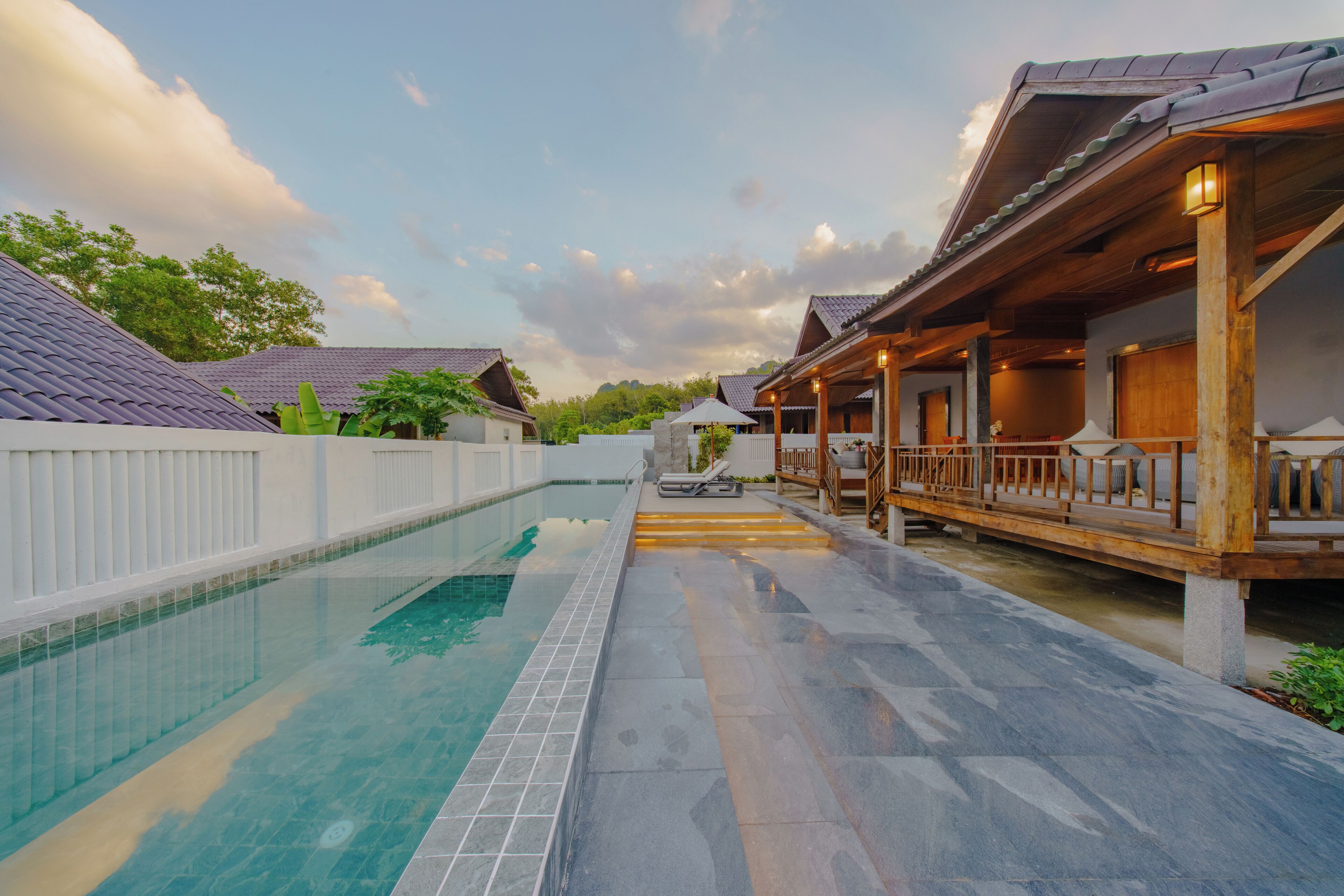 A swimming pool with a tiled deck, wooden deck with railings, and a covered area with seating.