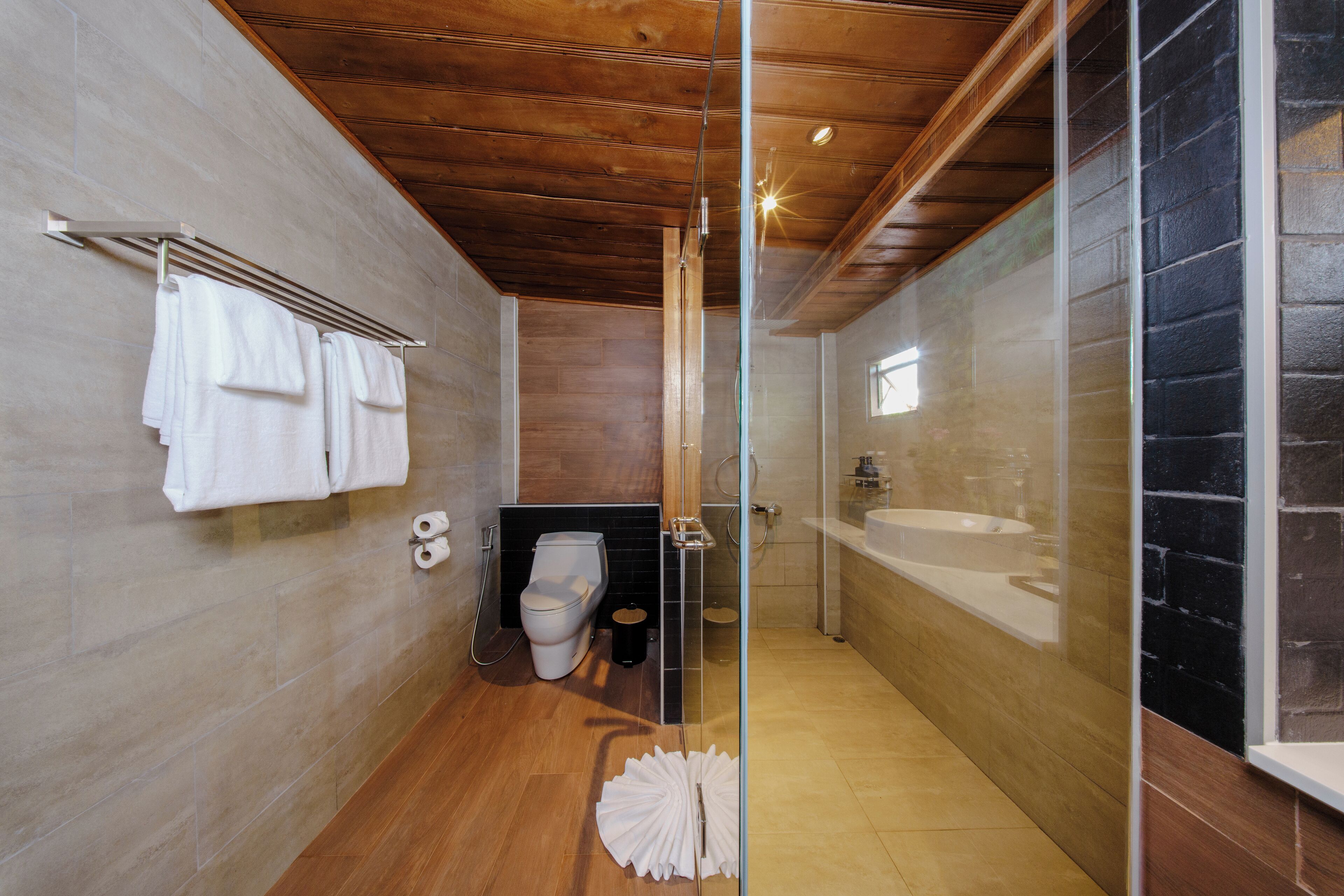 Une salle de bain moderne avec un plafond en bois, une cabine de douche en verre, un lavabo blanc et un porte-serviettes.