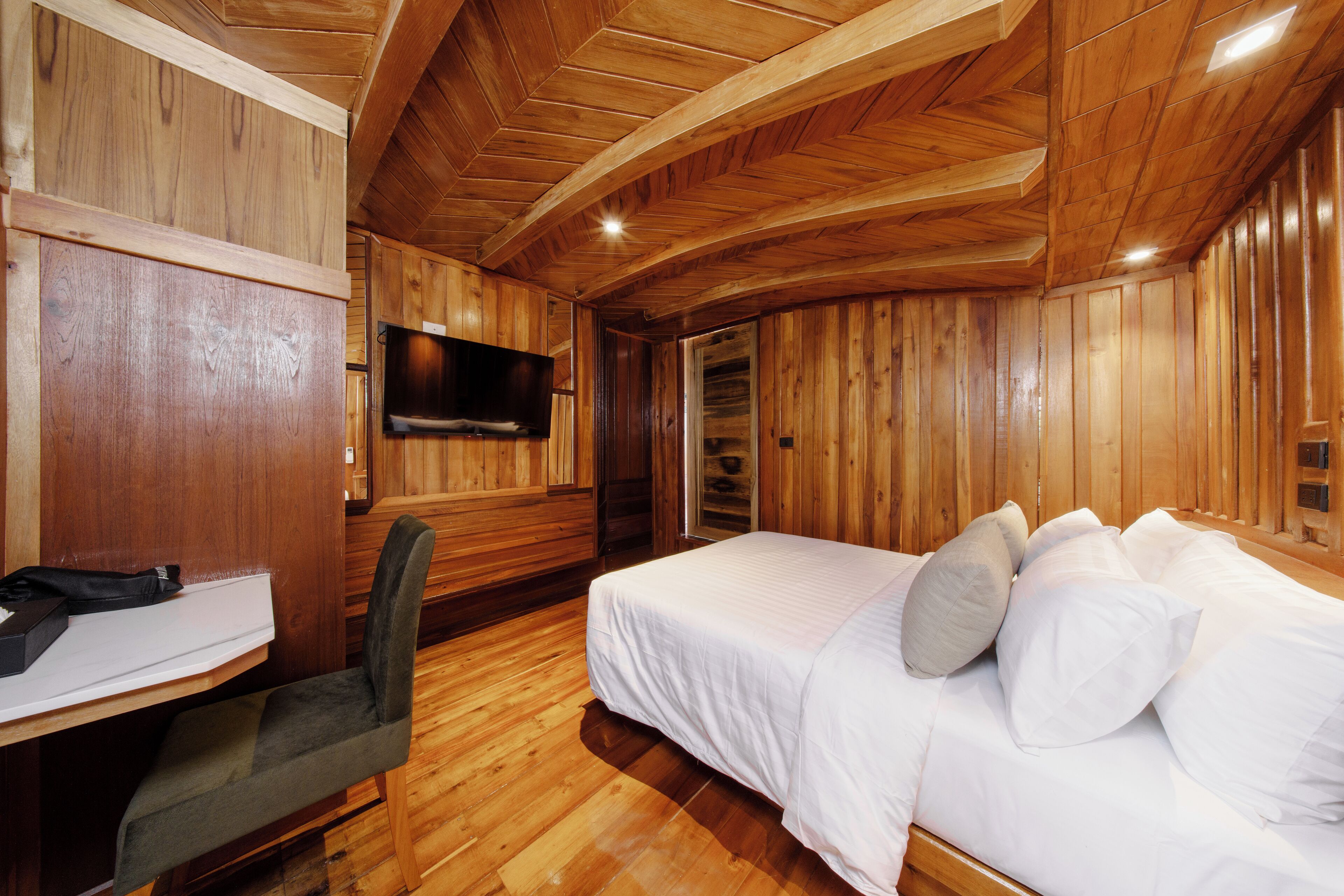 A wooden-paneled room with a bed, a desk, and a television.