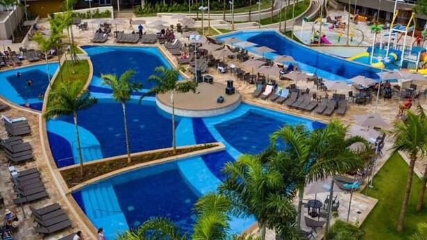A large outdoor swimming pool with multiple sections, surrounded by lounge chairs and palm trees. - RESORT: 2 adultos e 1 criança a 4km do Thermas Lar. e a 3km do Hot Beach (Olímpia)