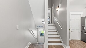 Ein modernes Interieur mit einer Treppe, die zu einer zweiten Etage führt, einem Flur mit einem Schild, das zum Strand weist, und einer Küchenzeile.