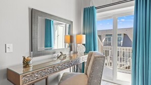 Ein Hotelzimmer mit einem großen Spiegel, einem Glastischchen mit Dekorationsobjekten, einem gepolsterten Sessel und Blick auf einen Balkon mit Geländer.