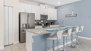 A modern kitchen with white cabinets, stainless steel appliances, and a bar area with bar stools. - Modern & cheerful, private pool, near Disney (Kissimmee)