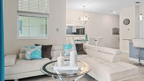A modern living room with a white sofa, a glass coffee table, and a dining area with a bar. - Modern & cheerful, private pool, near Disney (Kissimmee)