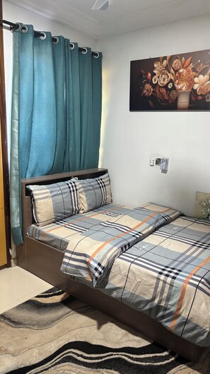 A bedroom with a bed, a nightstand, a wall-mounted air conditioner, and a painting of flowers. - CRL3 (Tema)