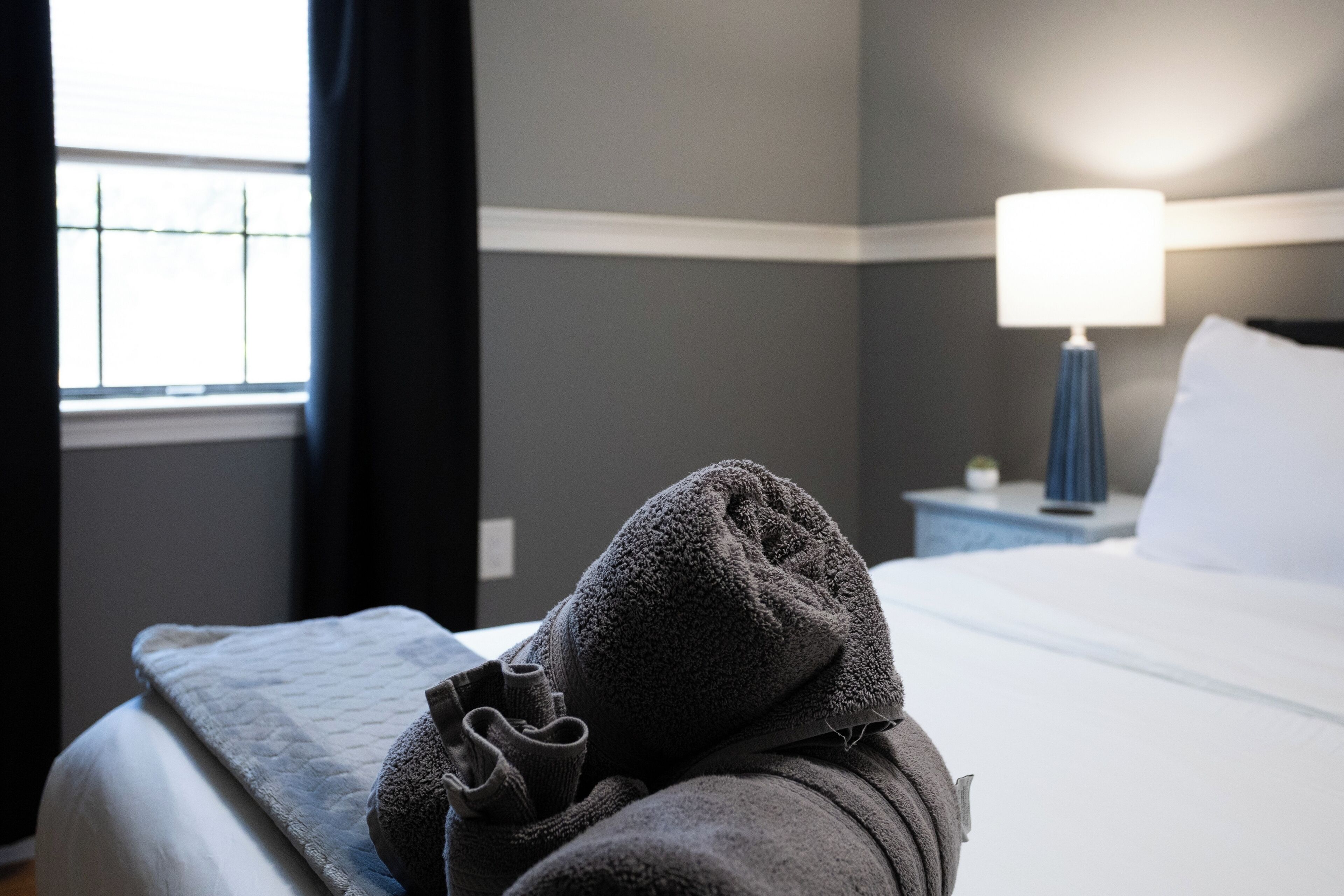 A neatly made bed with a white comforter and a folded gray towel on top.
