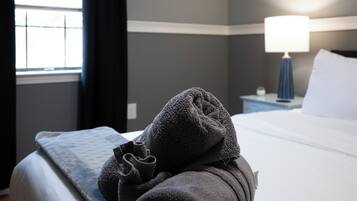 A neatly made bed with a white comforter and a folded gray towel on top.