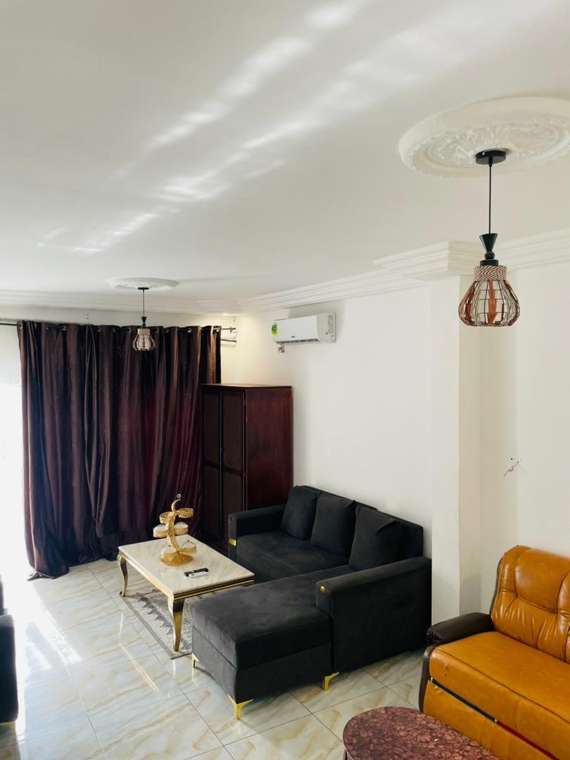 A living room with a black sofa, a brown leather armchair, a marble coffee table, and a hanging light fixture.