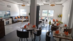 A modern dining area with round tables, dark chairs, and orange napkins. - Résidence hôtelière Samba (Douala)