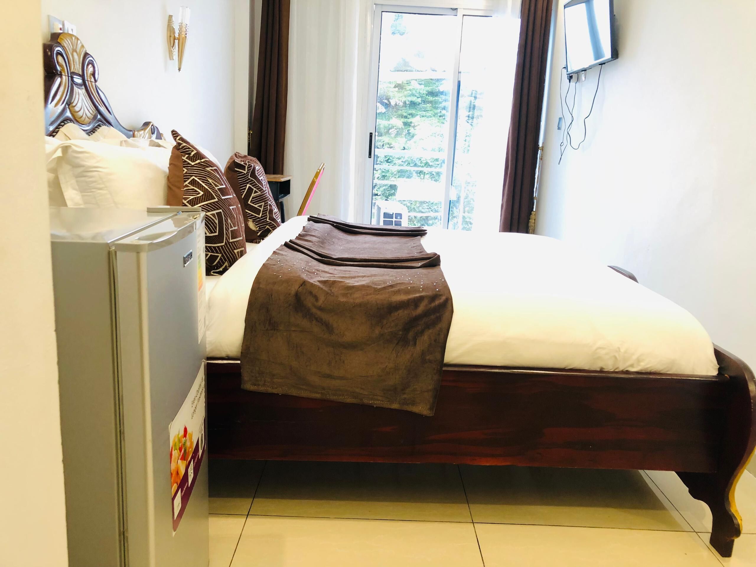 A neatly made bed with a brown bedspread, a wooden headboard, and patterned pillows. A small table with a lamp is beside the bed.