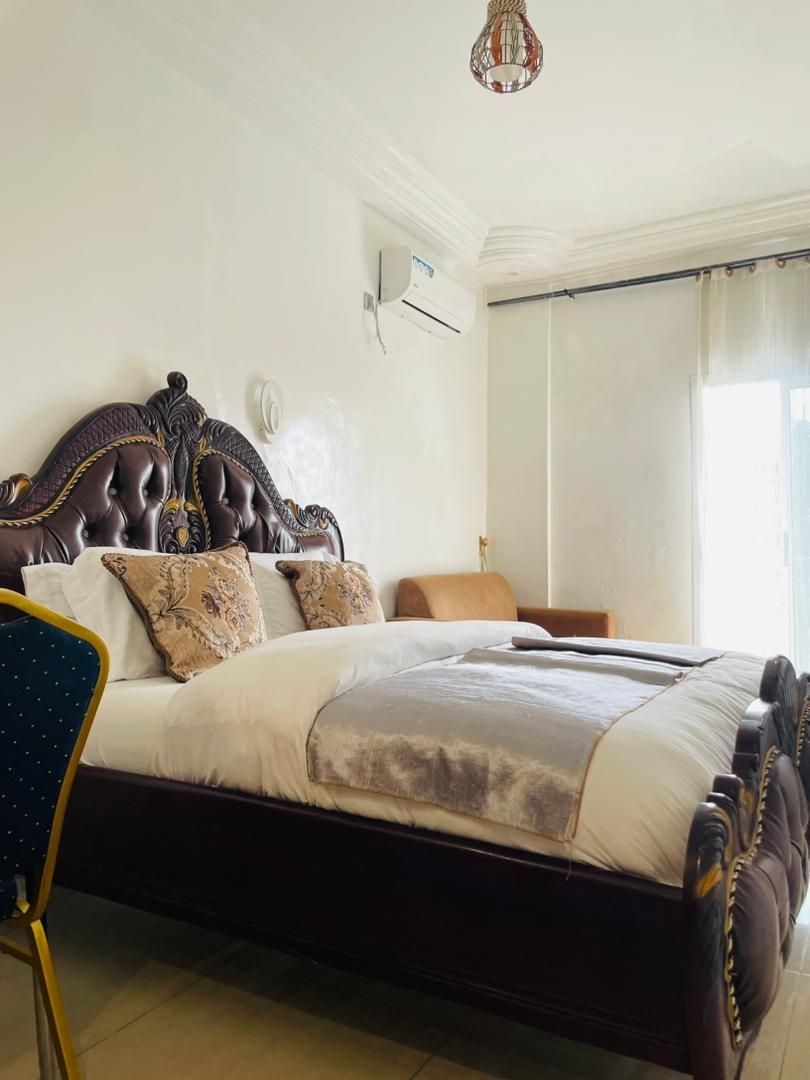 Un dormitorio con una cama grande, una silla, una lámpara en el techo y un ventanal con cortinas.