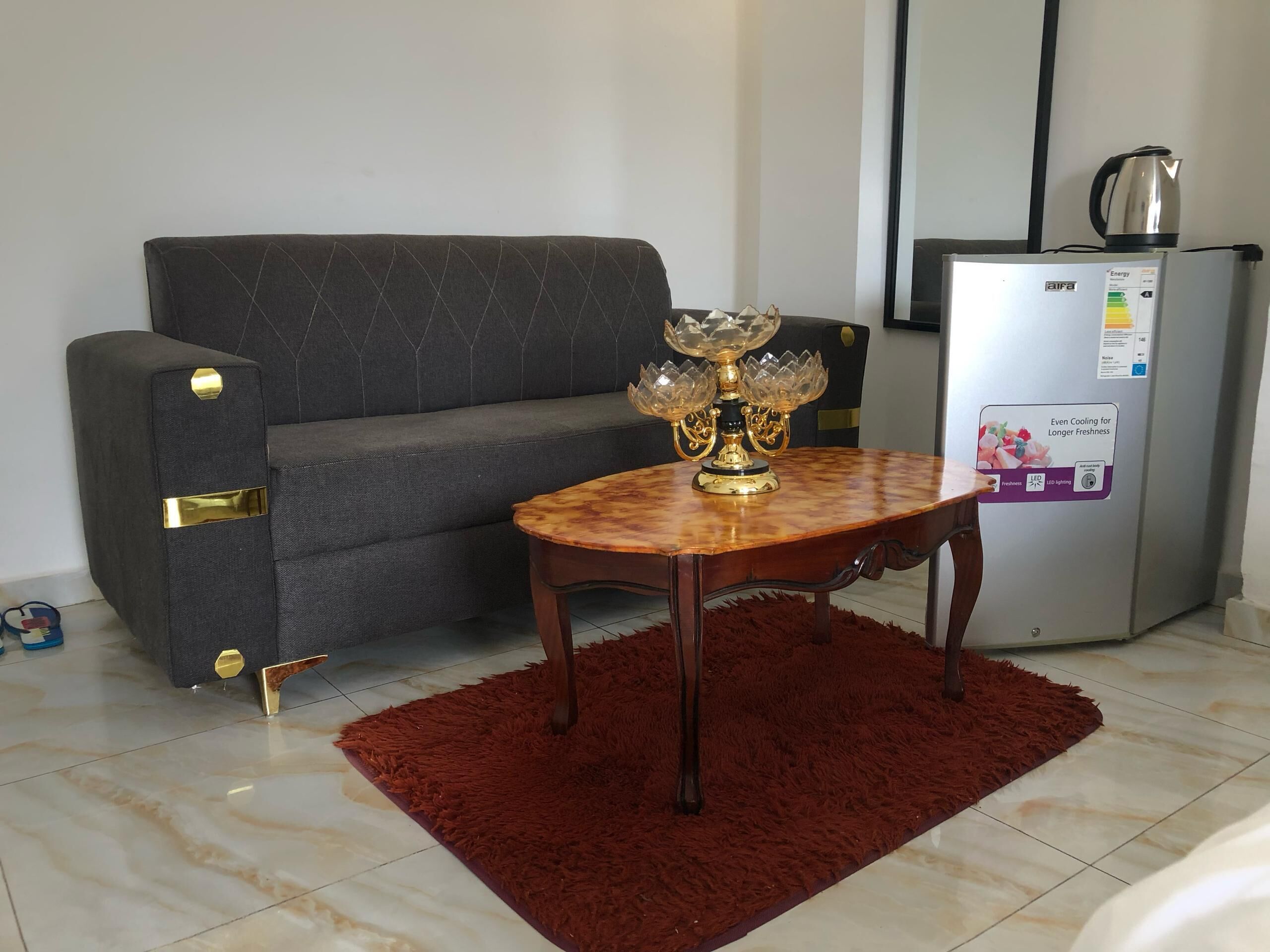A living room with a sofa, a table with a decorative centerpiece, a refrigerator, and a red rug.