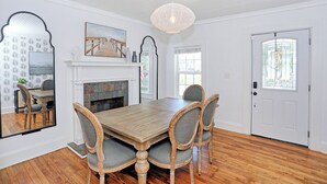 Une salle à manger avec une table en bois, quatre chaises, une cheminée et un grand miroir.