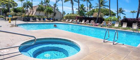 A swimming pool with a hot tub, surrounded by lounge chairs and palm trees.