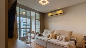 A modern living room with a sofa, a flat-screen TV, and a sliding glass door leading to a balcony. - 10 Minutes From the Olympic Park Pja802 (Rio de Janeiro)