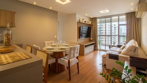 A modern living room with a sofa, a dining area with a table set for four, and a large window with a city view. - 10 Minutes From the Olympic Park Pja802 (Rio de Janeiro)