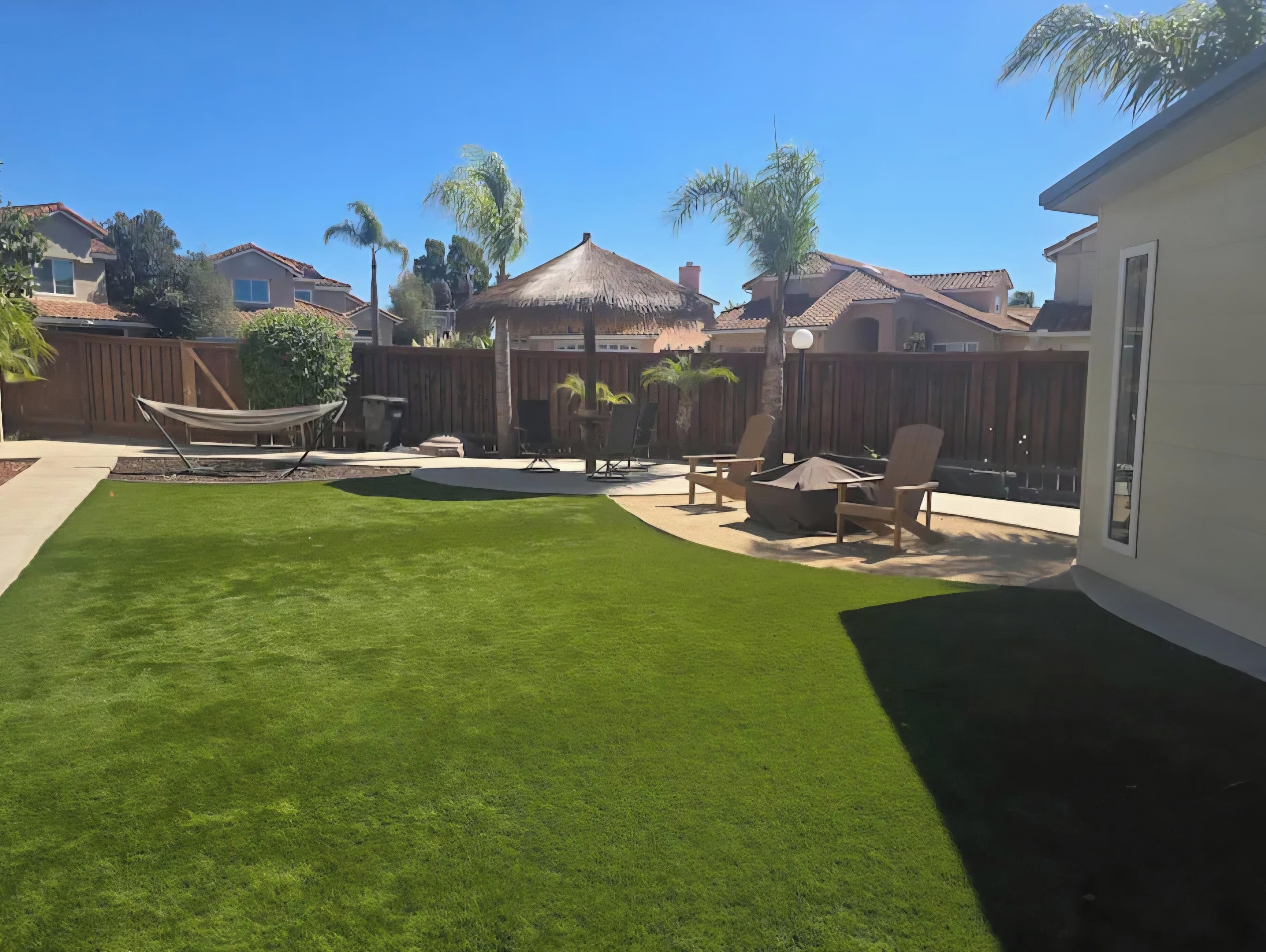 A backyard with a well-maintained lawn, a hammock, outdoor furniture, and a thatched-roof structure.