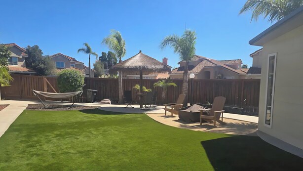 Un jardin avec une pelouse bien entretenue, un hamac, du mobilier de jardin et une structure dotée d’un toit de chaume.